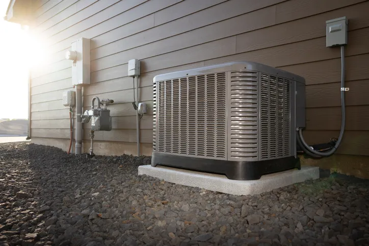 Outdoor AC unit on concrete pad beside house wall with utility boxes and cables.