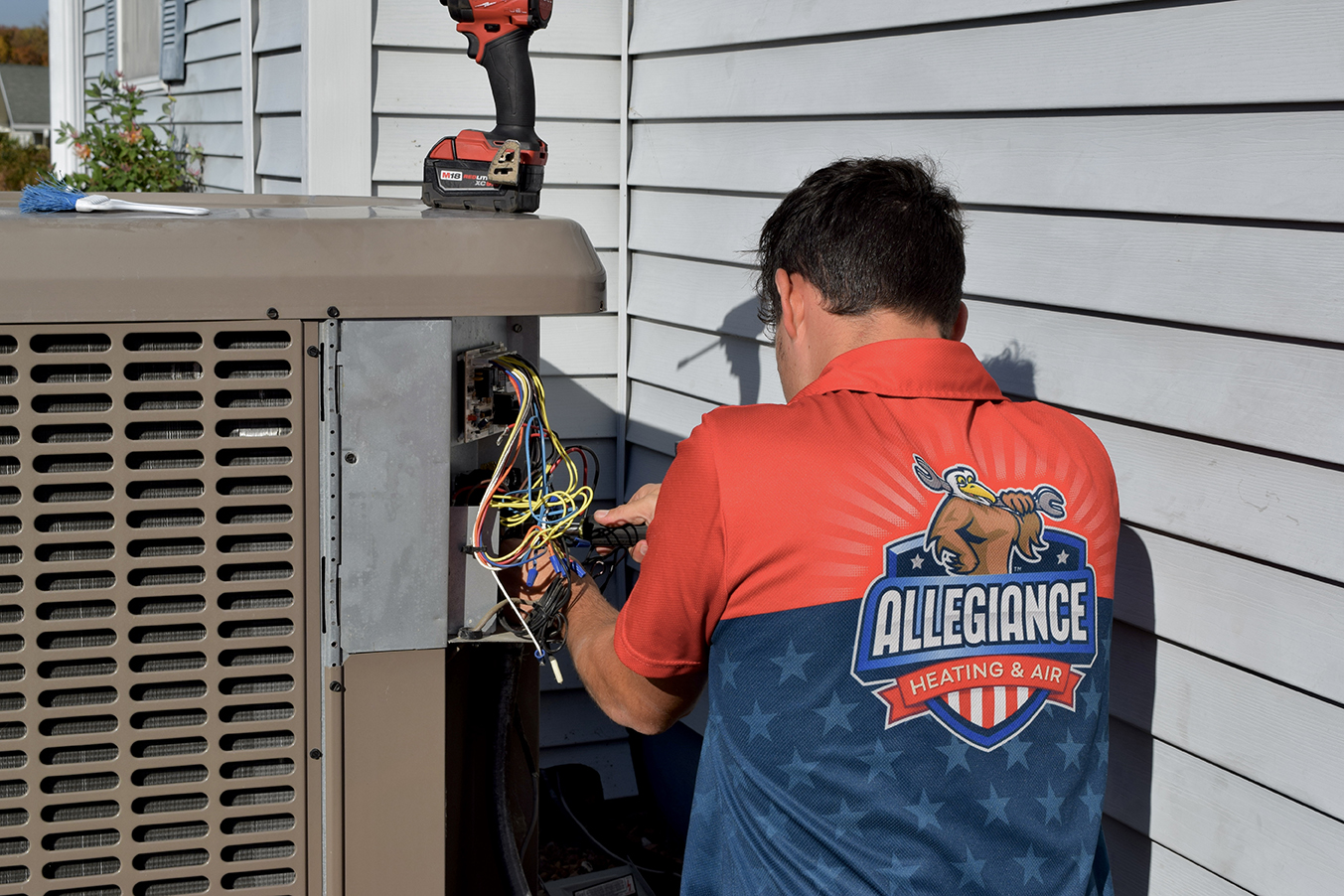 A technician wearing branded gear is repairing an Outdoor AC unit with hands and tools